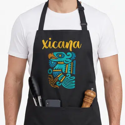 Chicano mexican apron - Yellow Xicana text above blue and yellow abstract indigenous bird-like graphic — shown on a black cotton canvas apron against a white background