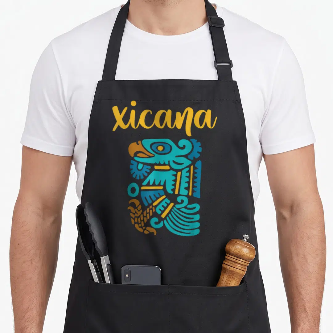 Chicano mexican apron - Yellow Xicana text above blue and yellow abstract indigenous bird-like graphic — shown on a black cotton canvas apron against a white background