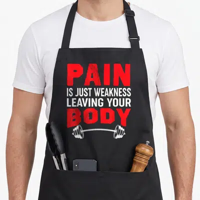Weakness body apron - PAIN IS JUST WEAKNESS LEAVING YOUR BODY text in red and white above a barbell illustration — shown on a black cotton canvas apron against a white background