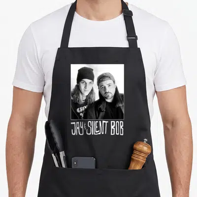 Silent jay lover apron - Grayscale photo of two men with JAY and SILENT BOB text below — shown on a black cotton canvas apron against a white background