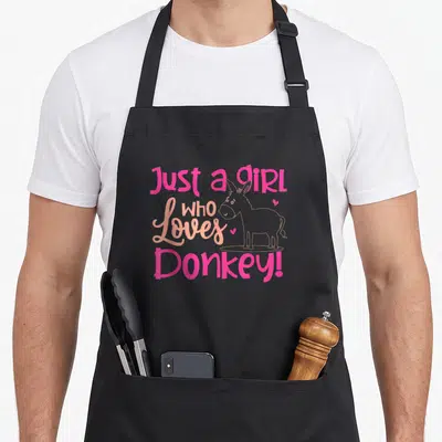 Outfit donkey lover apron - Pink and peach cartoon donkey with stacked text and small hearts on grey background — shown on a black cotton canvas apron against a white background