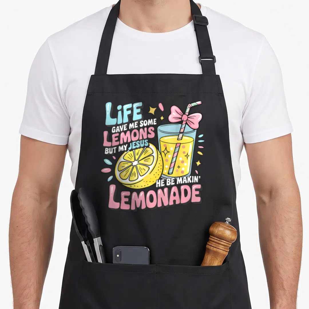 Makin lemonade apron - Cartoon lemonade glass with pink bow and life gave me lemons text — shown on a black cotton canvas apron against a white background
