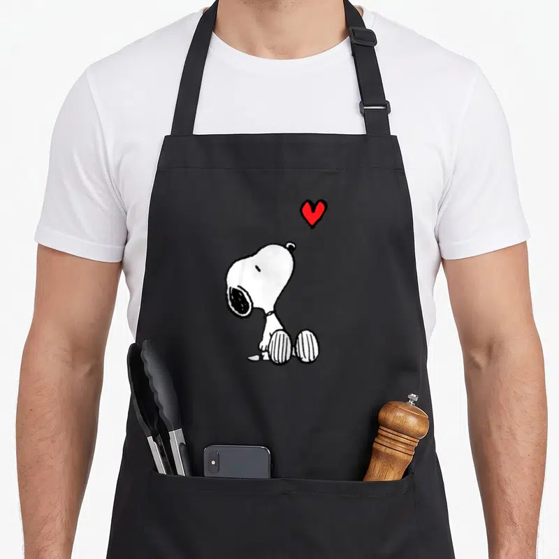 Valentine baseball apron - Snoopy sitting in black and white looking up at a small red heart floating above his head — shown on a black cotton canvas apron against a white background