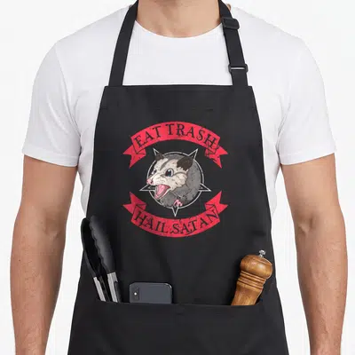 Eat satay apron - Cartoon opossum in white pentagram with red ribbons reading EAT TRASH HAIL SATAN — shown on a black cotton canvas apron against a white background