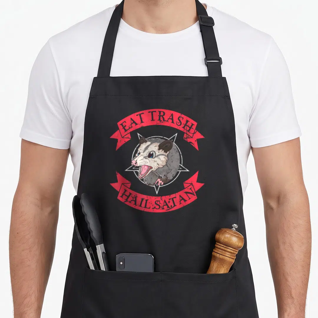 Eat satay apron - Cartoon opossum in white pentagram with red ribbons reading EAT TRASH HAIL SATAN — shown on a black cotton canvas apron against a white background