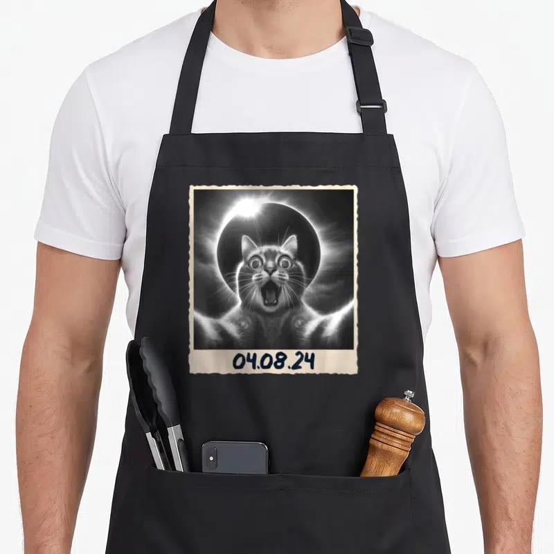Solar funny cat apron - Polaroid photo of a surprised cat in front of a solar eclipse with date 04.08.24 — shown on a black cotton canvas apron against a white background
