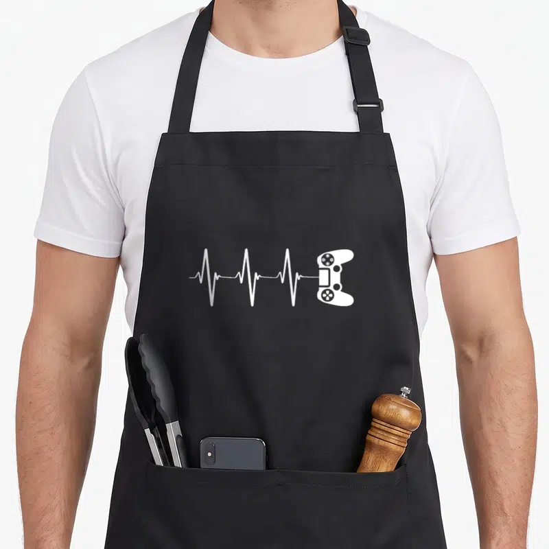 Pulse video game apron - White heartbeat line connecting to a game controller in minimalist style — shown on a black cotton canvas apron against a white background