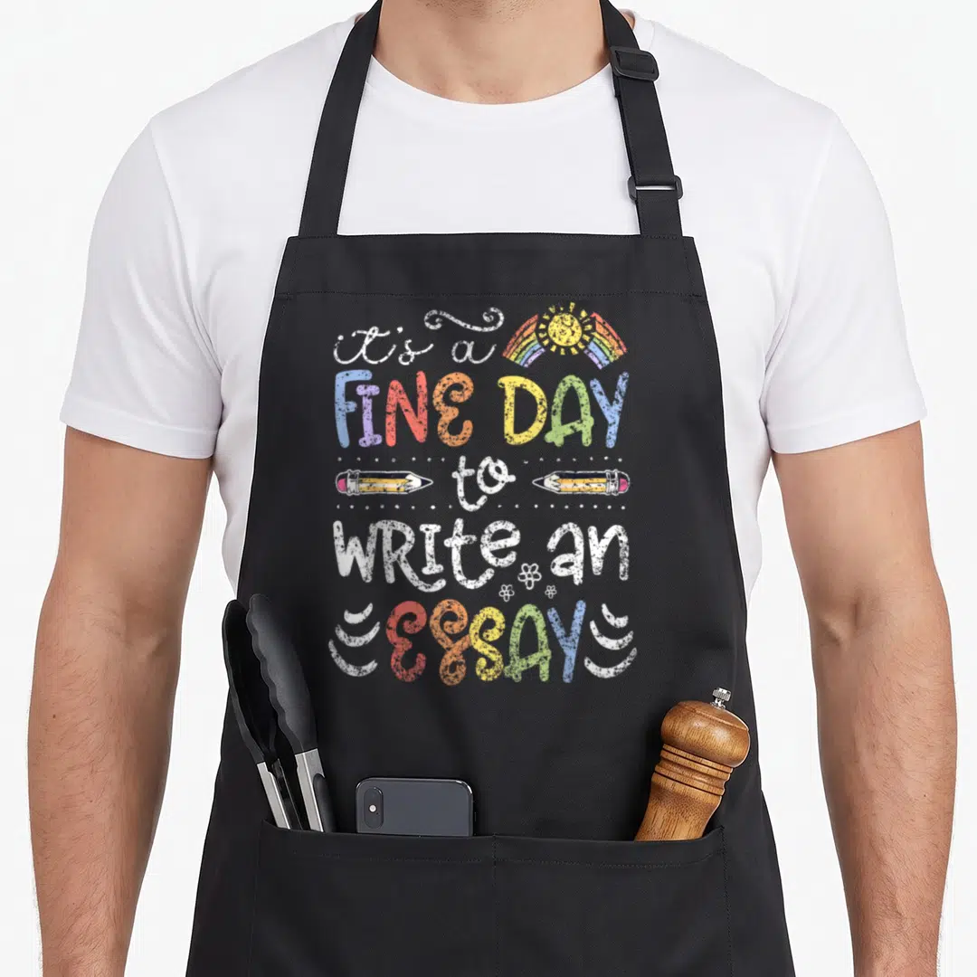 Fine english chef apron - Stacked text it's a FINE DAY to WRITE AN ESSAYS with rainbow sun and two pencils — shown on a black cotton canvas apron against a white background