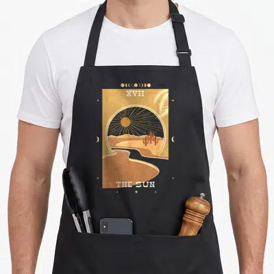 Dark boho apron - XVII THE SUN tarot desert scene with sun cactus river moon phases stars in tan brown yellow white — shown on a black cotton canvas apron against a white background
