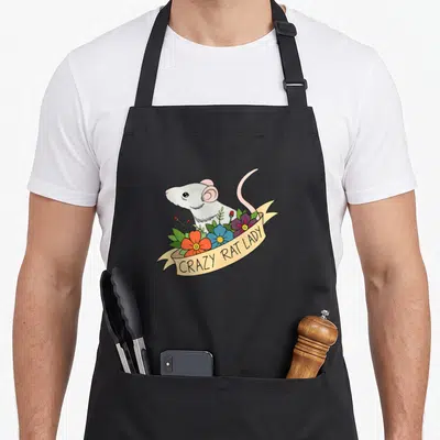 Flower rodent pet apron - Cartoon white rat behind orange blue and purple flowers on beige ribbon — shown on a black cotton canvas apron against a white background