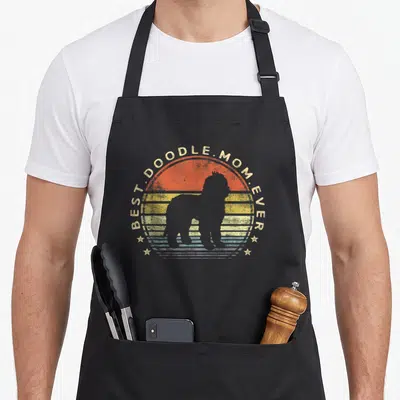 Labradoodle goldendoodle dog apron - Retro sunset circle with BEST.DOODLE.MOM.EVER text and grey dog silhouette — shown on a black cotton canvas apron against a white background