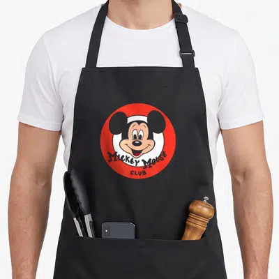 Retro friends apron - Red circle with Mickey Mouse face and curved MICKEY MOUSE CLUB text — shown on a black cotton canvas apron against a white background