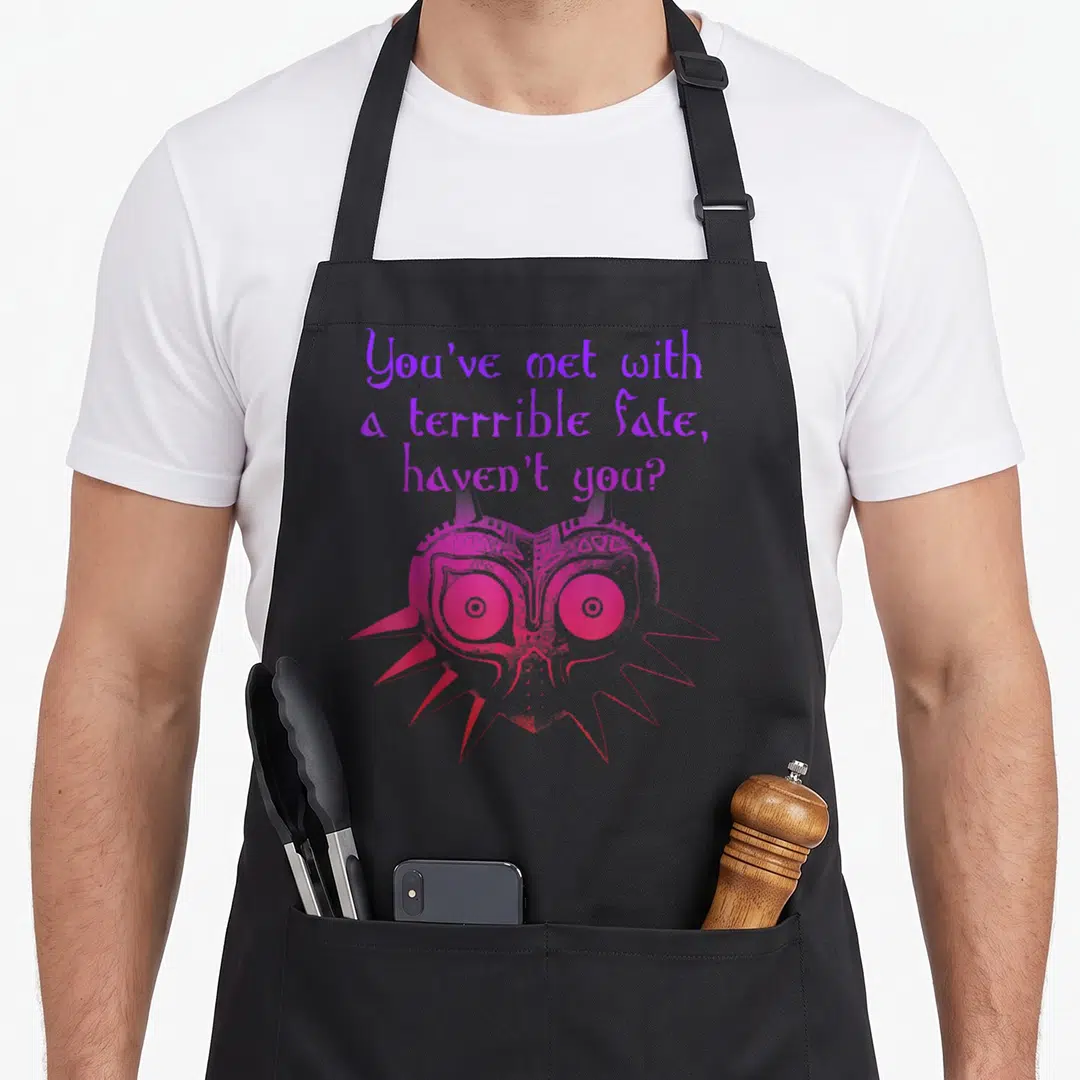 Terrible mets apron - Purple text reading You've met with a terrible fate above a pink and red stylized mask — shown on a black cotton canvas apron against a white background
