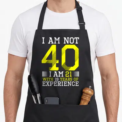Birthday 40th apron for women - Yellow 40 and white text I am not 40 I am 21 with 19 years of experience on black — shown on a black cotton canvas apron against a white background