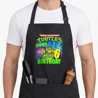 Mademark teenage cooking aprons - Teenage Mutant Ninja Turtles cartoon with It's my 6 BIRTHDAY text and large yellow — shown on a black cotton canvas apron against a white background