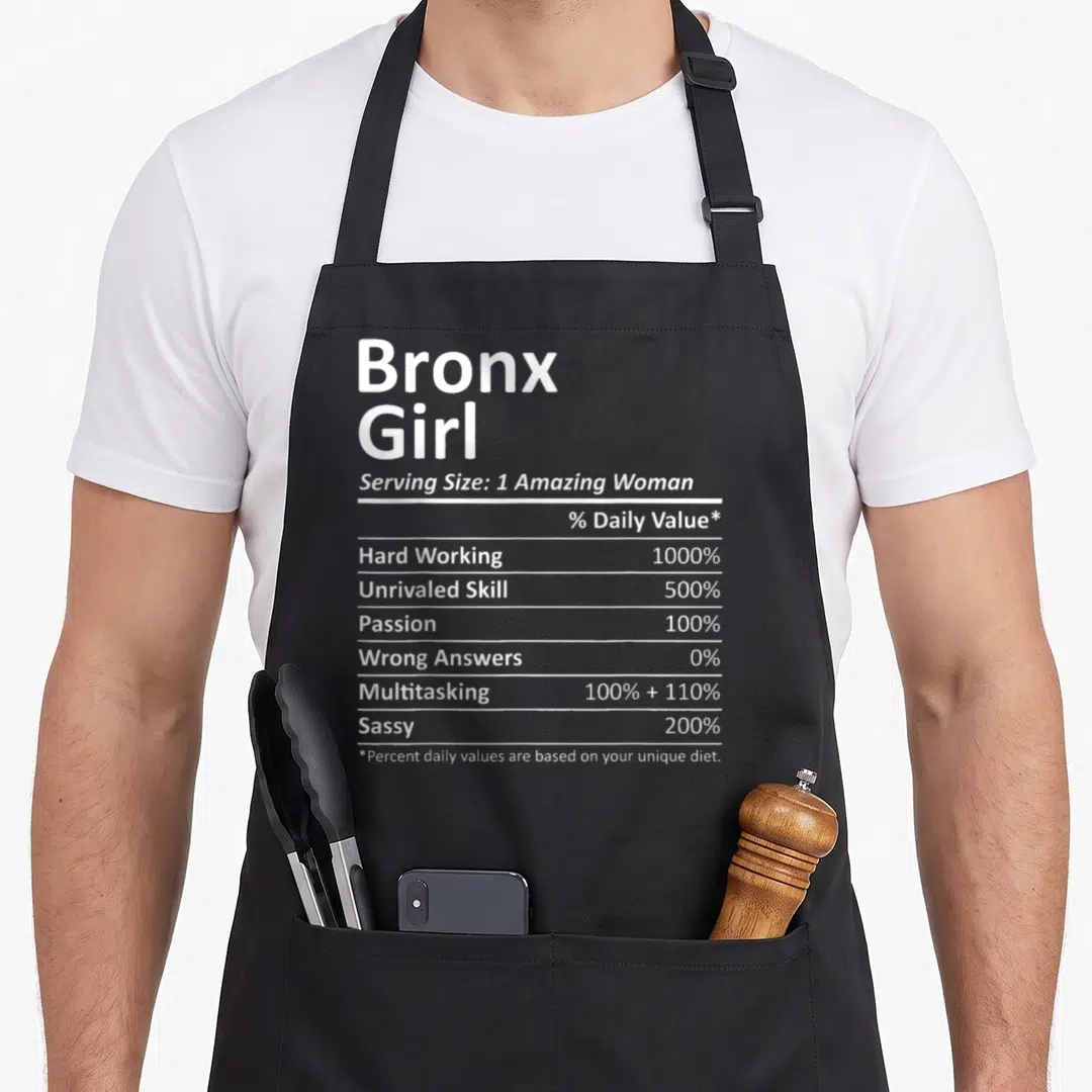 Bronx root new york apron - White typography on gray background formatted as a nutrition facts label listing Bronx Girl — shown on a black cotton canvas apron against a white background