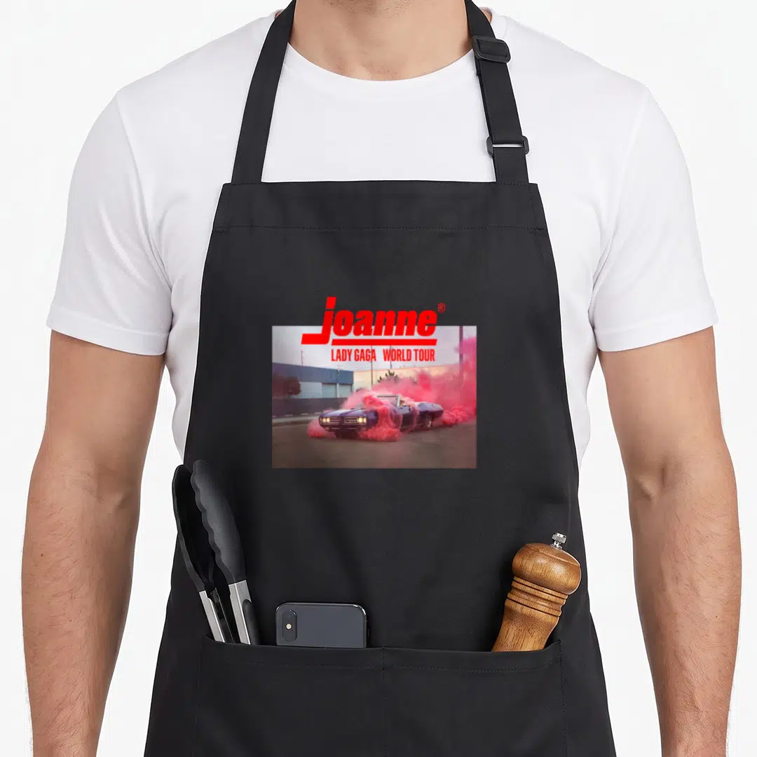 Joanne world music apron - Red joanne text above purple car in pink smoke in front of blue building — shown on a black cotton canvas apron against a white background