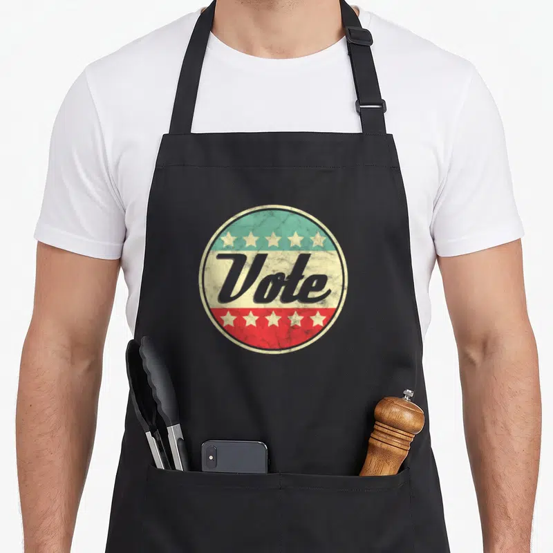 Right midterms apron - RetroVote text on cream band inside circle with teal top, red bottom, and five white stars — shown on a black cotton canvas apron against a white background