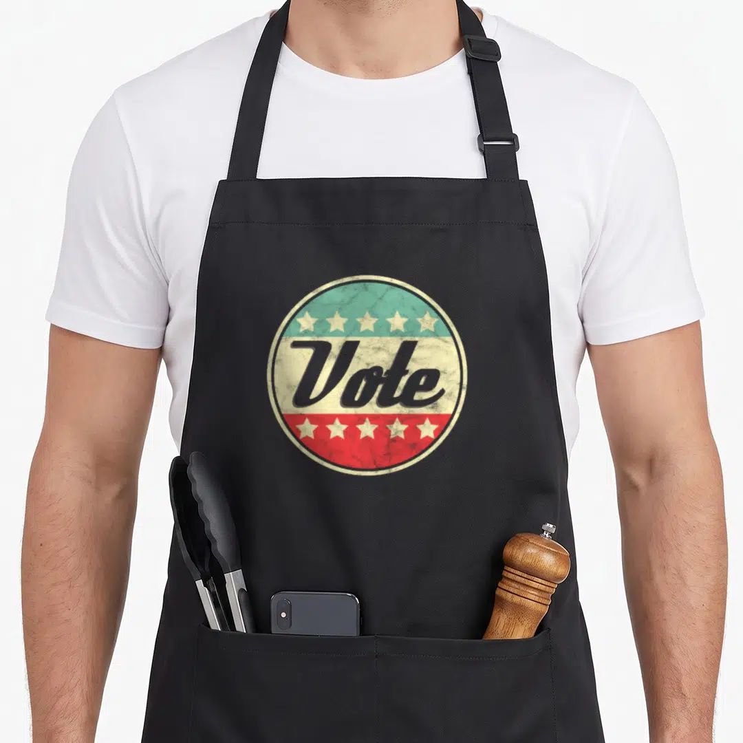 Right midterms apron - RetroVote text on cream band inside circle with teal top, red bottom, and five white stars — shown on a black cotton canvas apron against a white background