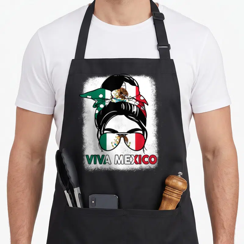 Viva mexico apron - Woman with flag bandana and sunglasses displaying Viva Mexico text in distressed green white red — shown on a black cotton canvas apron against a white background