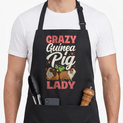 Comfort crazy guinea lady apron - Two cartoon guinea pigs under stacked pink and beige text reading CRAZY Guinea Pig — shown on a black cotton canvas apron against a white background