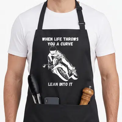 Curve motorcycle apron - White distressed text and motorcyclist leaning on bike with split layout — shown on a black cotton canvas apron against a white background