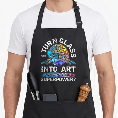 Glass artist stained apron - Distressed white text around a circular stained glass butterfly in blue yellow red — shown on a black cotton canvas apron against a white background