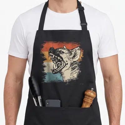 Zoo african apron - Distressed hyena head graphic over four horizontal stripes in beige orange yellow and teal — shown on a black cotton canvas apron against a white background