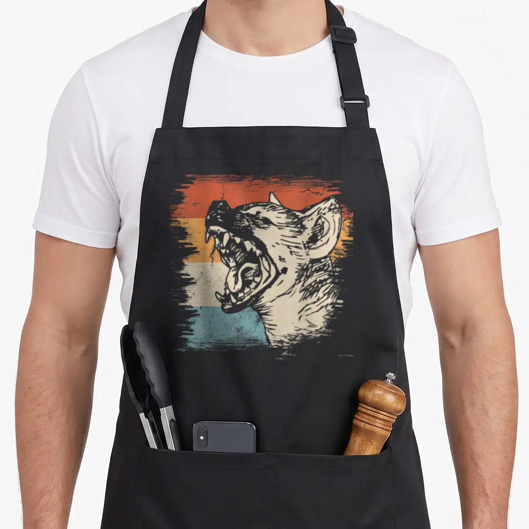 Zoo african apron - Distressed hyena head graphic over four horizontal stripes in beige orange yellow and teal — shown on a black cotton canvas apron against a white background
