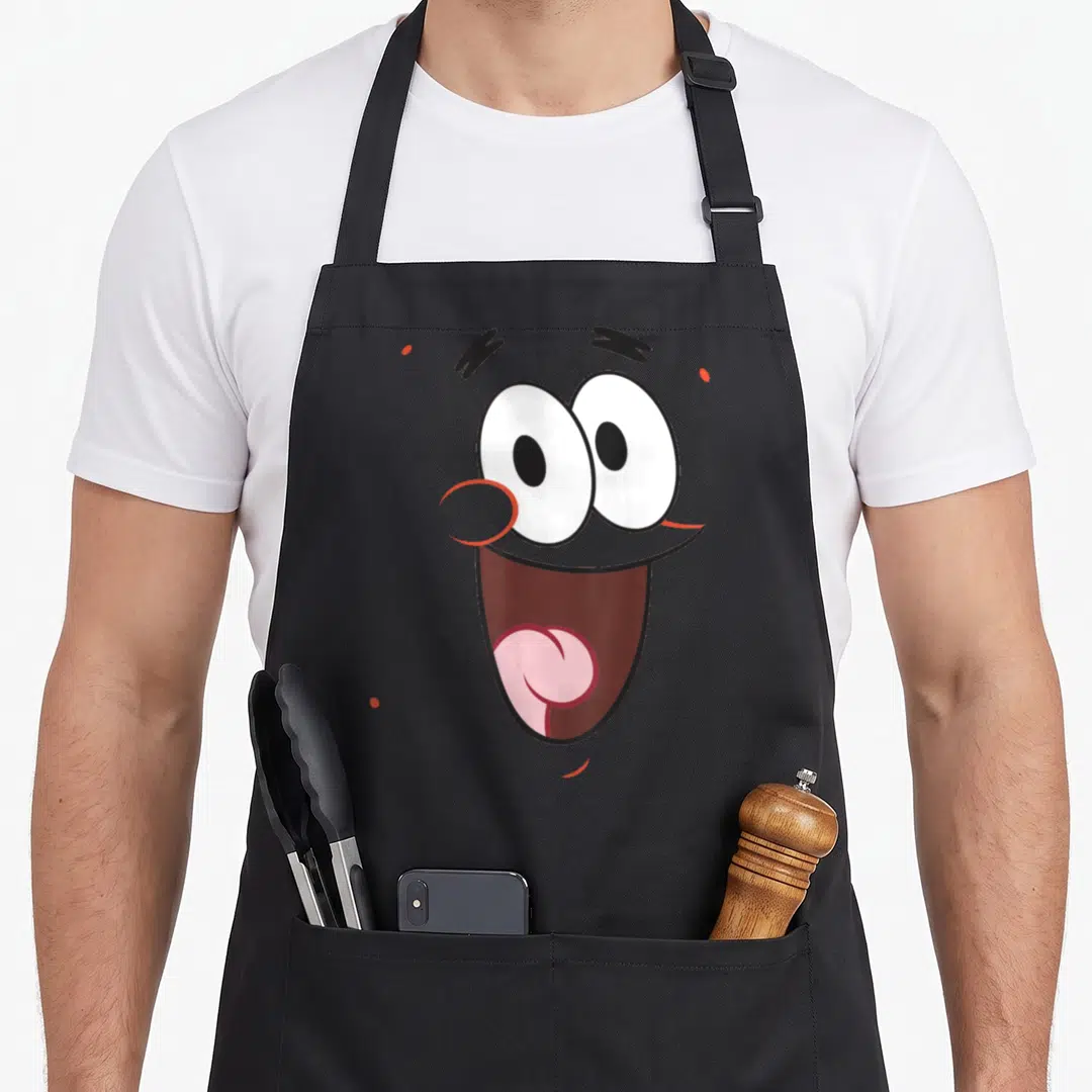 Squarepant halloween white apron - Cartoon face with large white eyes, pink tongue, and brown mouth on grey background — shown on a black cotton canvas apron against a white background