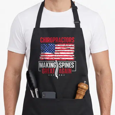 Chiropractor making aprons - Distressed USA flag with white spine graphic and red white blue text CHIROPRACTORS MAKING — shown on a black cotton canvas apron against a white background