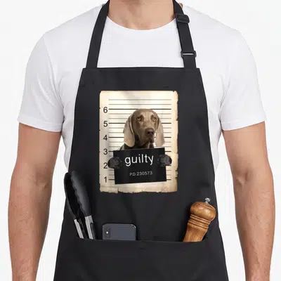 Weimaraner dog apron - Grey dog holding black sign with text guilty P.D.230573 in front of height chart — shown on a black cotton canvas apron against a white background
