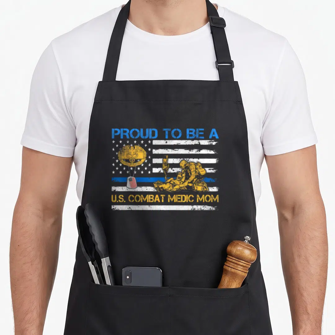 Combat military apron - Distressed flag with combat medic scene, medical emblem, dog tags, and proud mom text in blue — shown on a black cotton canvas apron against a white background