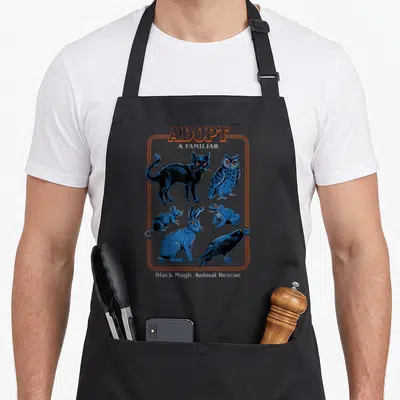 Steven magic apron - ADOPT A FAMILIAR text above six blue cartoon animals in an orange border — shown on a black cotton canvas apron against a white background