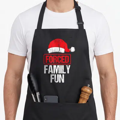Forced winter apron - Distressed red Santa hat above stamped FORCED FAMILY FUN text in red and white — shown on a black cotton canvas apron against a white background