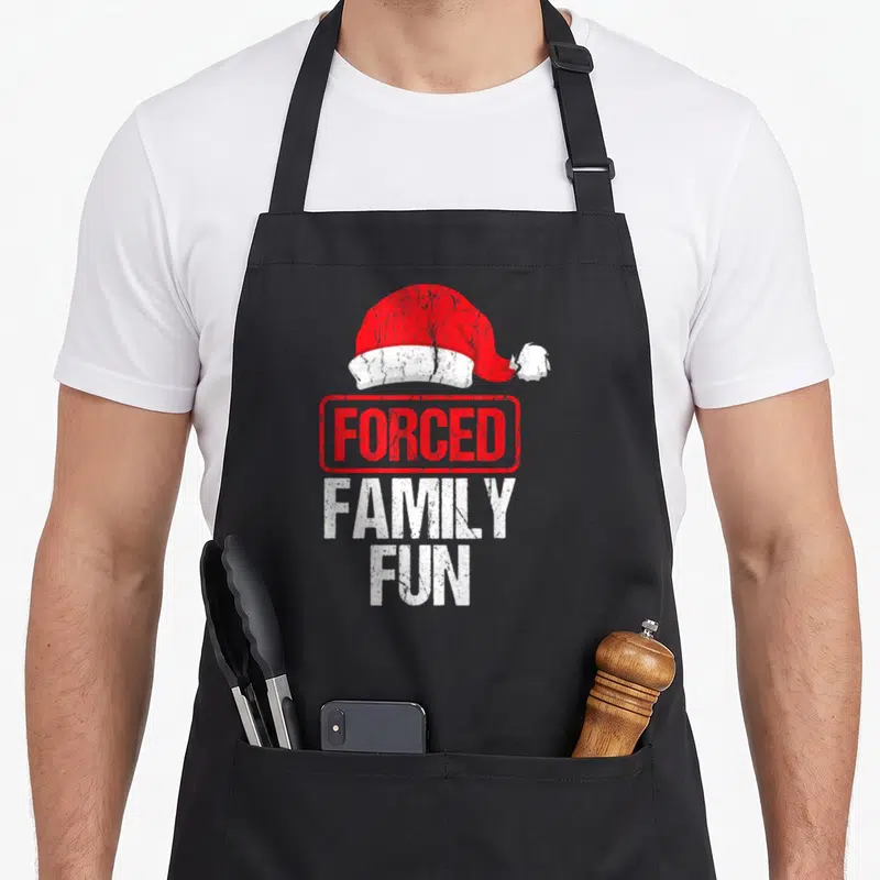 Forced winter apron - Distressed red Santa hat above stamped FORCED FAMILY FUN text in red and white — shown on a black cotton canvas apron against a white background