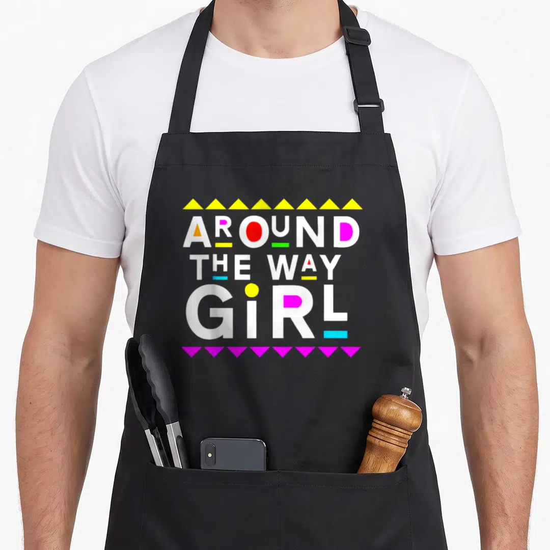 Around 90s apron - Stacked white text AROUND THE WAY GIRL with yellow top triangles, magenta bottom triangles — shown on a black cotton canvas apron against a white background