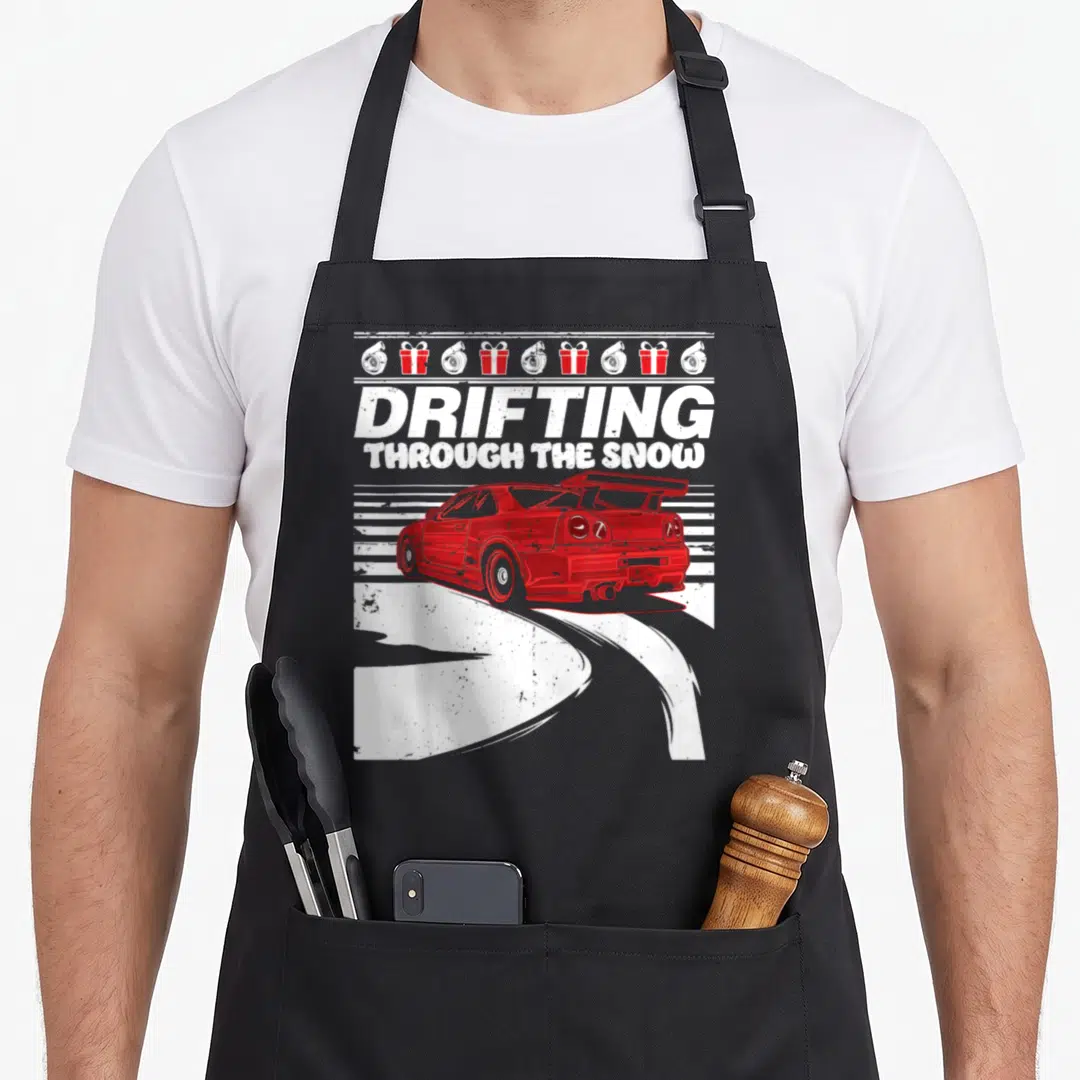 Car design imports vintage apron - Red car drifting left with DRIFTING THROUGH THE SNOW text and turbo gift box row — shown on a black cotton canvas apron against a white background