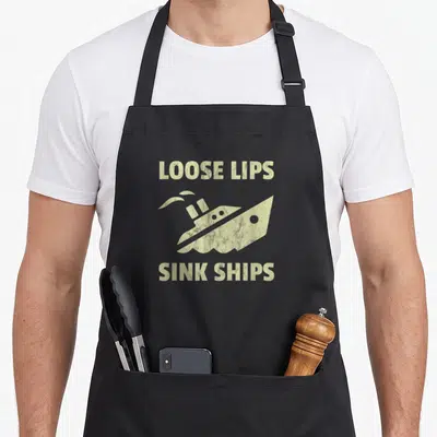 Lip loose funny apron - Beige LOOSE LIPS SINK SHIPS text with a tilted ship silhouette between two lines of distressed — shown on a black cotton canvas apron against a white background