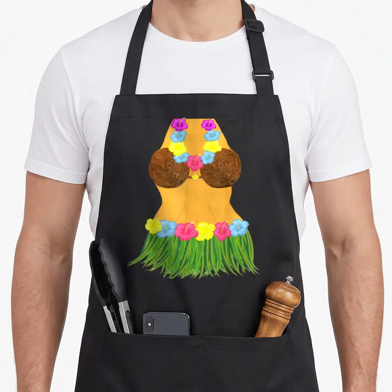 Coconut skirt apron - Cartoon tan torso with brown coconut bra, green grass skirt, and colorful hibiscus lei — shown on a black cotton canvas apron against a white background