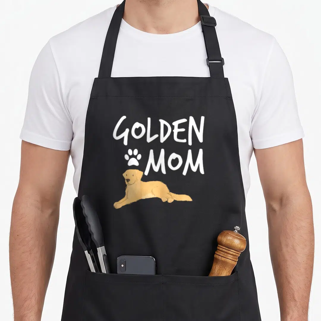 Dog puppy golden retriever apron - Cartoon golden dog lying under white GOLDEN MOM text and paw print — shown on a black cotton canvas apron against a white background