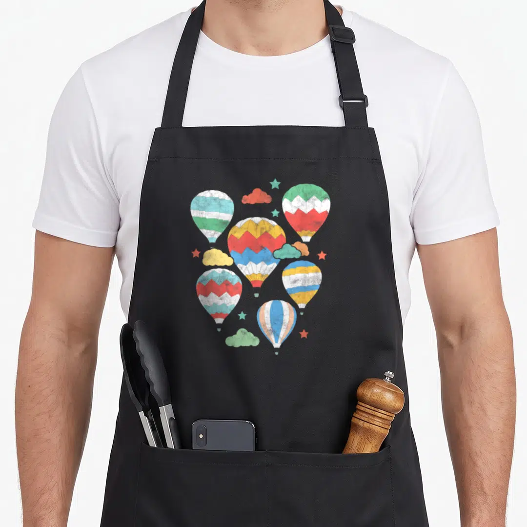 Hot air balloon apron - Six striped hot air balloons in blue red yellow green and white with clouds and stars — shown on a black cotton canvas apron against a white background