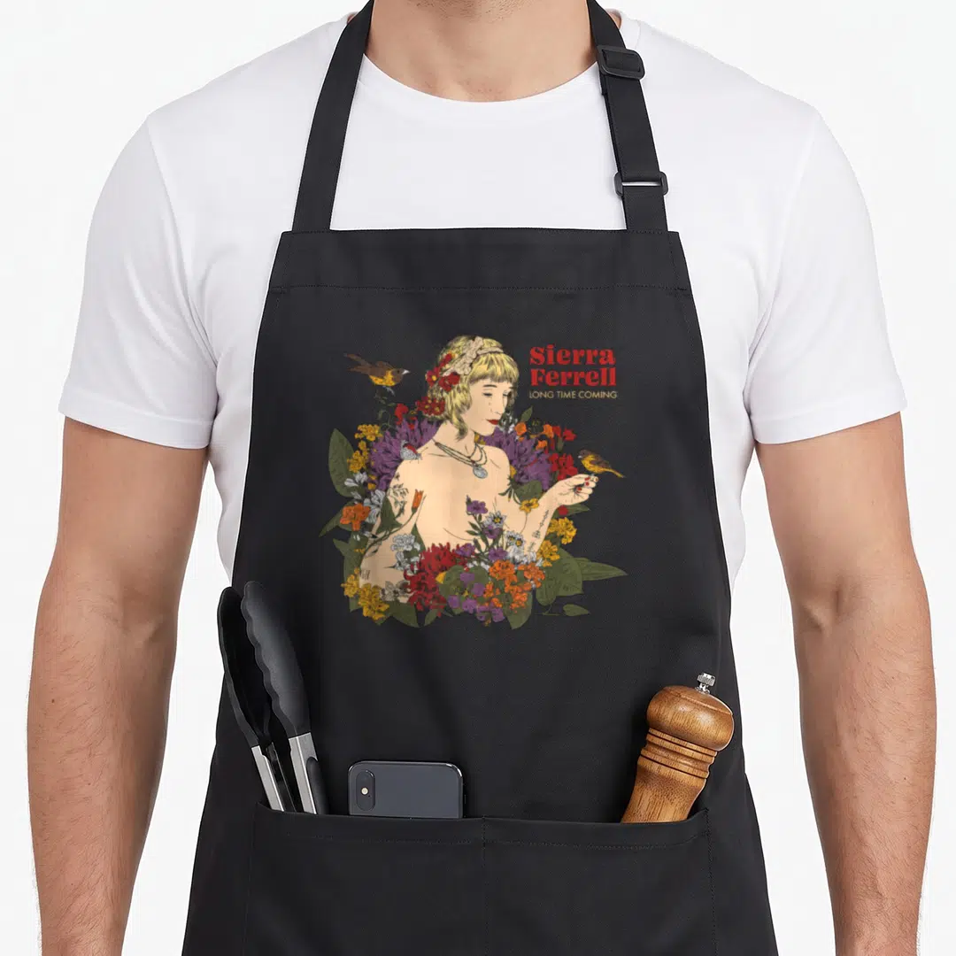 Ferrell sierra apron - Line-art woman surrounded by red yellow green purple flowers with two perched birds and stacked — shown on a black cotton canvas apron against a white background