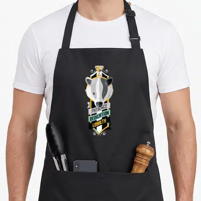 Patience hufflepuff apron - Badger head over shield with three banners reading PATIENCE DEDICATION LOYALTY in grey — shown on a black cotton canvas apron against a white background
