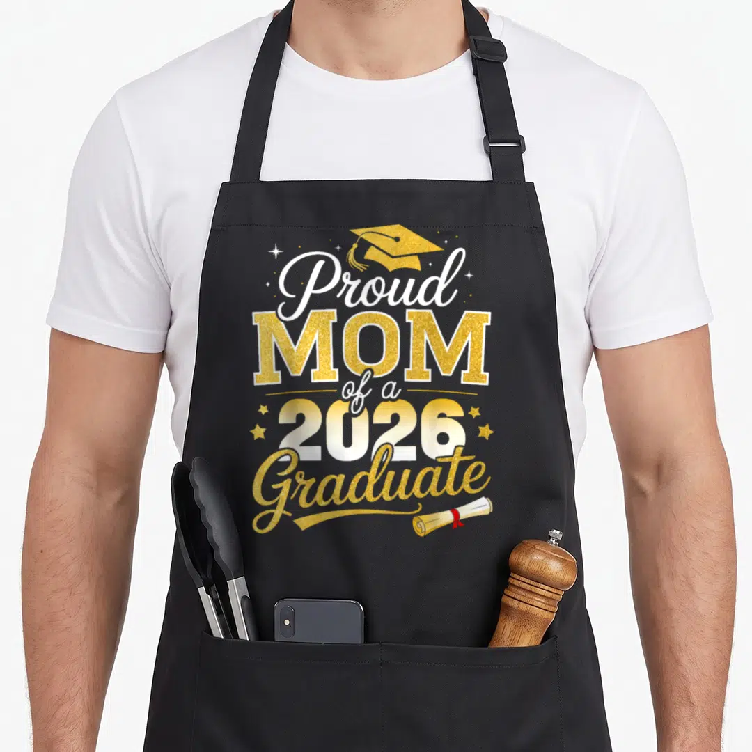 Proud grade graduation apron - Gold and white text Proud MOM 2026 Graduate with cap and scroll icons — shown on a black cotton canvas apron against a white background