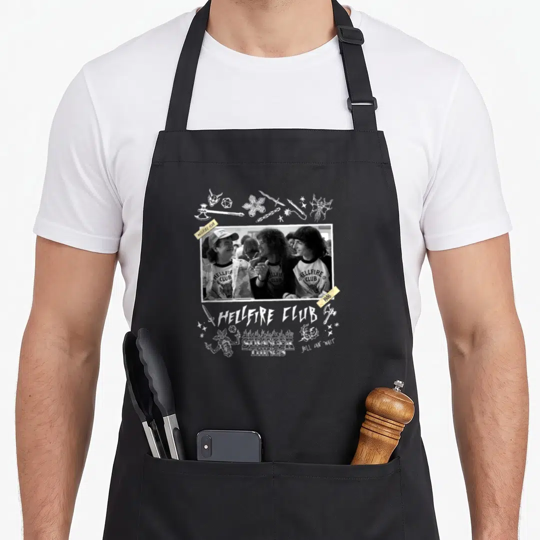 Yearbook novelty apron - Grayscale photo of three people with Hellfire Club text and white fantasy line art on yellow — shown on a black cotton canvas apron against a white background