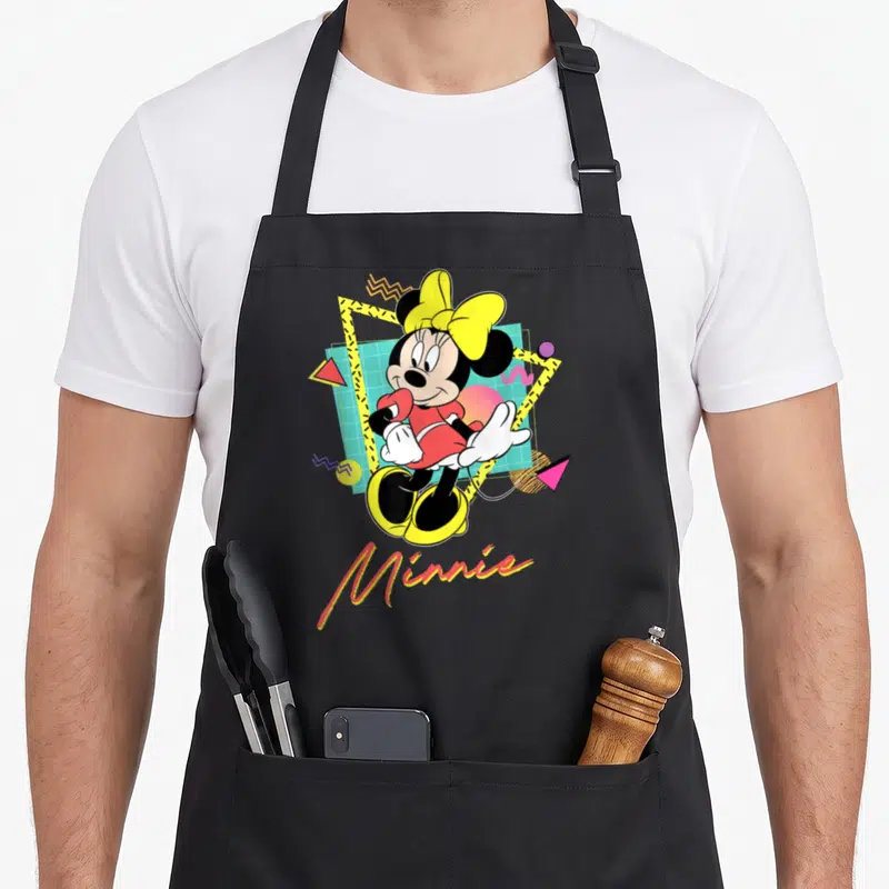 90s couple apron - Cartoon Minnie Mouse over cyan grid with yellow bow and geometric shapes — shown on a black cotton canvas apron against a white background