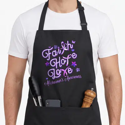 Alzheimer ribbon apron - Faith Hope Love text with purple ribbons, flowers, butterflies, and hearts curved Alzheimer's — shown on a black cotton canvas apron against a white background