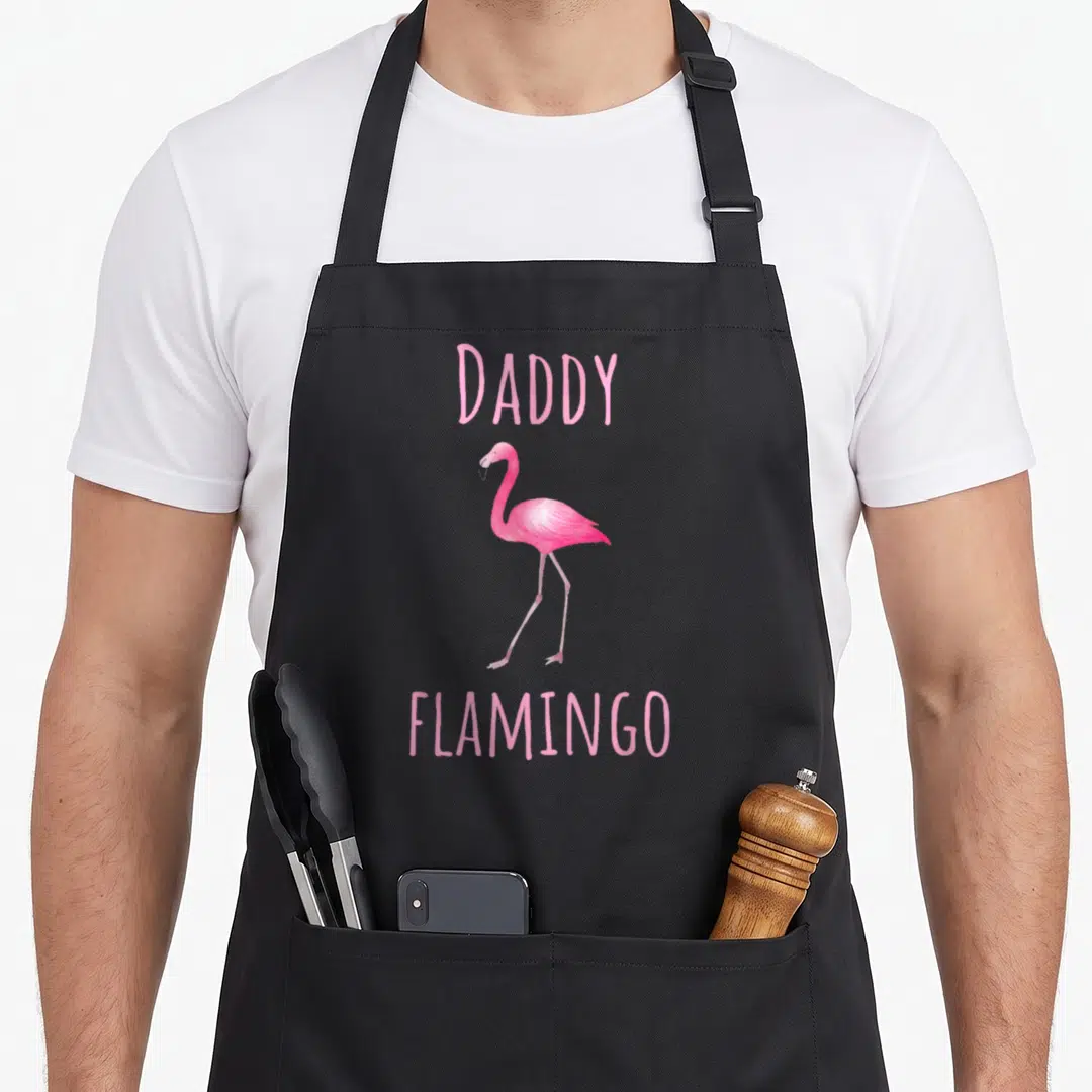 Daddy pink flamingo apron - Watercolor pink flamingo standing between the words Daddy and Flamingo in pink text — shown on a black cotton canvas apron against a white background