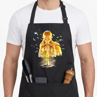 Breath watercolors apron - Golden elf with praying hands above a glowing sword and scattered leaves in yellow and white — shown on a black cotton canvas apron against a white background